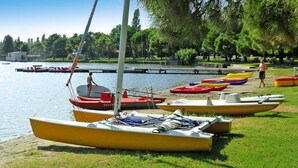 A row of small boats lined up on a grassy shore by a calm body of water, with a dock and trees in the background. - Club Village & Hotel Spiaggia Romea, Lido Delle Nazioni (Comacchio)