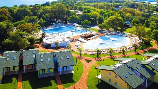 An aerial view of a resort with multiple swimming pools, a central fountain, and a variety of buildings with flat roofs. - Club Village & Hotel Spiaggia Romea, Lido Delle Nazioni (Comacchio)