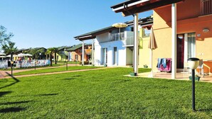 A residential building with a balcony, a covered outdoor seating area, and a well-maintained lawn. - Club Village & Hotel Spiaggia Romea, Lido Delle Nazioni (Comacchio)