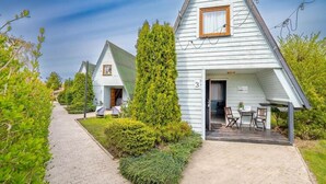 A row of white cabins with a paved walkway and greenery. Each cabin has a door and a window.