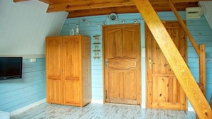 A room with wooden ceilings and walls, a wooden door, and a television mounted on the wall.