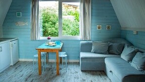 A cozy room with a blue wall, a window with curtains, a dining table with chairs, and a gray sofa.