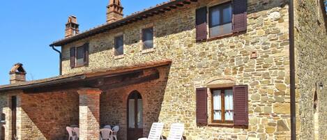 A stone building with a patio area, outdoor seating, and a clear sky.