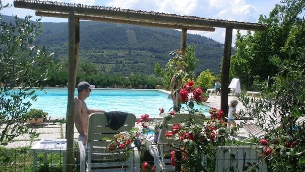 A poolside area with a pergola, outdoor seating, and a view of a mountain landscape. - Romantic studio apartment with a view (Toscana)