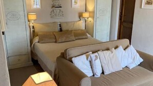 A bedroom with a bed, a sofa, two bedside lamps, and a wall-mounted shelf with decorative items. - Romantic studio apartment with a view (Toscana)