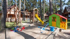 A playground with a slide, swings, and sand area, surrounded by wooden cabins. - Apartment in Pobierowo Near Baltic Beach (Rewal)