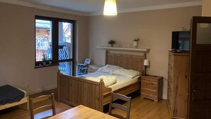 A room with a wooden bed, a table, a chair, a TV on a cabinet, and a window with a view of an outdoor area. - Apartment in Pobierowo Near Baltic Beach (Rewal)