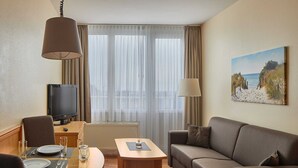 A hotel room with a wooden dining table, a sofa, a TV, and a painting on the wall. - Appartements im Freizeitpark Weissenhauser Strand (Wangels)