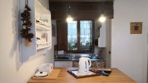 Une petite cuisine avec une table en bois, une bouilloire et une étagère contenant des ustensiles de cuisine.