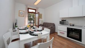 A modern kitchen with white cabinets, a built-in oven, and a dining area with a white table set for four. - Residenza Rocca del Lago (Riva del Garda)
