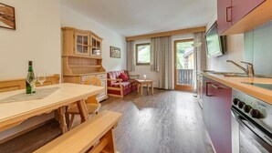 Una zona de estar acogedora con una mesa de madera para comer, bancos, un sofá y una cocina con estufa y armarios.