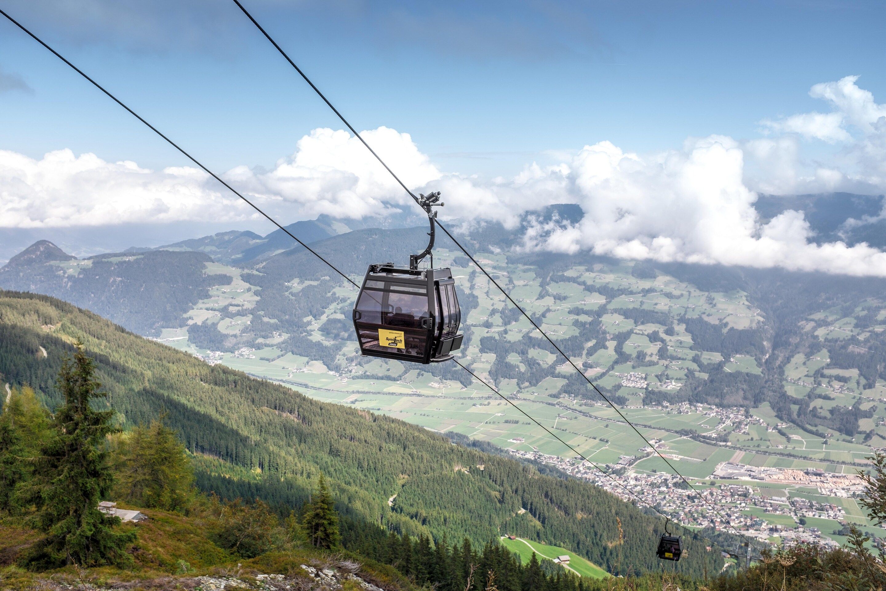 Eine Seilbahn über einer gebirgigen Landschaft, darunter eine Stadt.