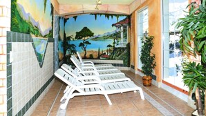 Un solárium con un mural de un paisaje, suelo de baldosas y varios sillones.