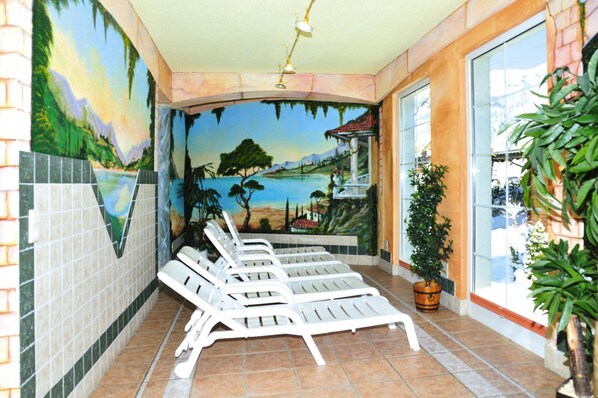 Uma sala de sol com um mural de paisagem, piso de azulejos e várias poltronas.