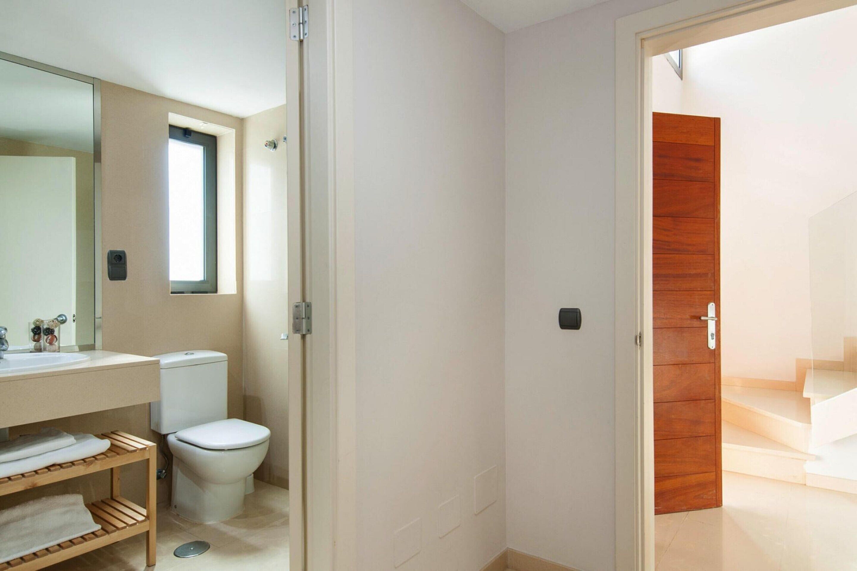 Un baño moderno con inodoro, lavamanos y estante de madera.