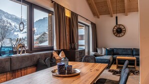 Ein gemütliches Wohnzimmer mit einem Holzesstisch, einem blauen Sofa und einem großen Fenster mit Blick auf schneebedeckte Hügel.