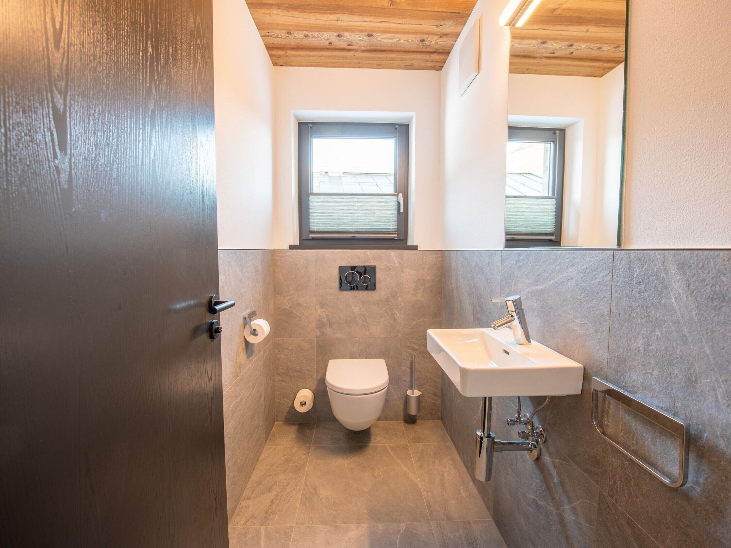 A modern bathroom with a toilet, sink, and a window above the sink.