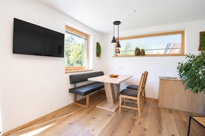 A compact living space with a flat-screen TV mounted on the wall, a bench, a dining table with chairs, and a small window with a view of trees. - Holiday Home in Aschau by Zillertal Alps (Aschau Im Zillertal)