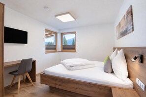 Une chambre à coucher avec un lit, un bureau et deux fenêtres donnant sur des arbres et des montagnes.