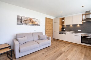 Een moderne keuken met een inbouwoven en een koffieapparaat, een beige bank en een houten eettafel.