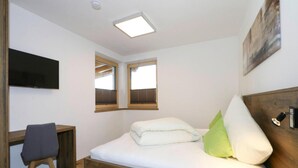 Une chambre à coucher avec un lit en bois, un bureau, une chaise, un téléviseur et deux fenêtres équipées de stores.