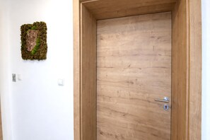 Een houten deur met een eenvoudig handvat en een sleutelgat, een klein lichtschakelaartje op de muur en een decoratief stuk mos.