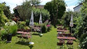 Un jardin extérieur agrémenté de tables et de chaises, entouré d’une végétation luxuriante et de plantes en fleurs.