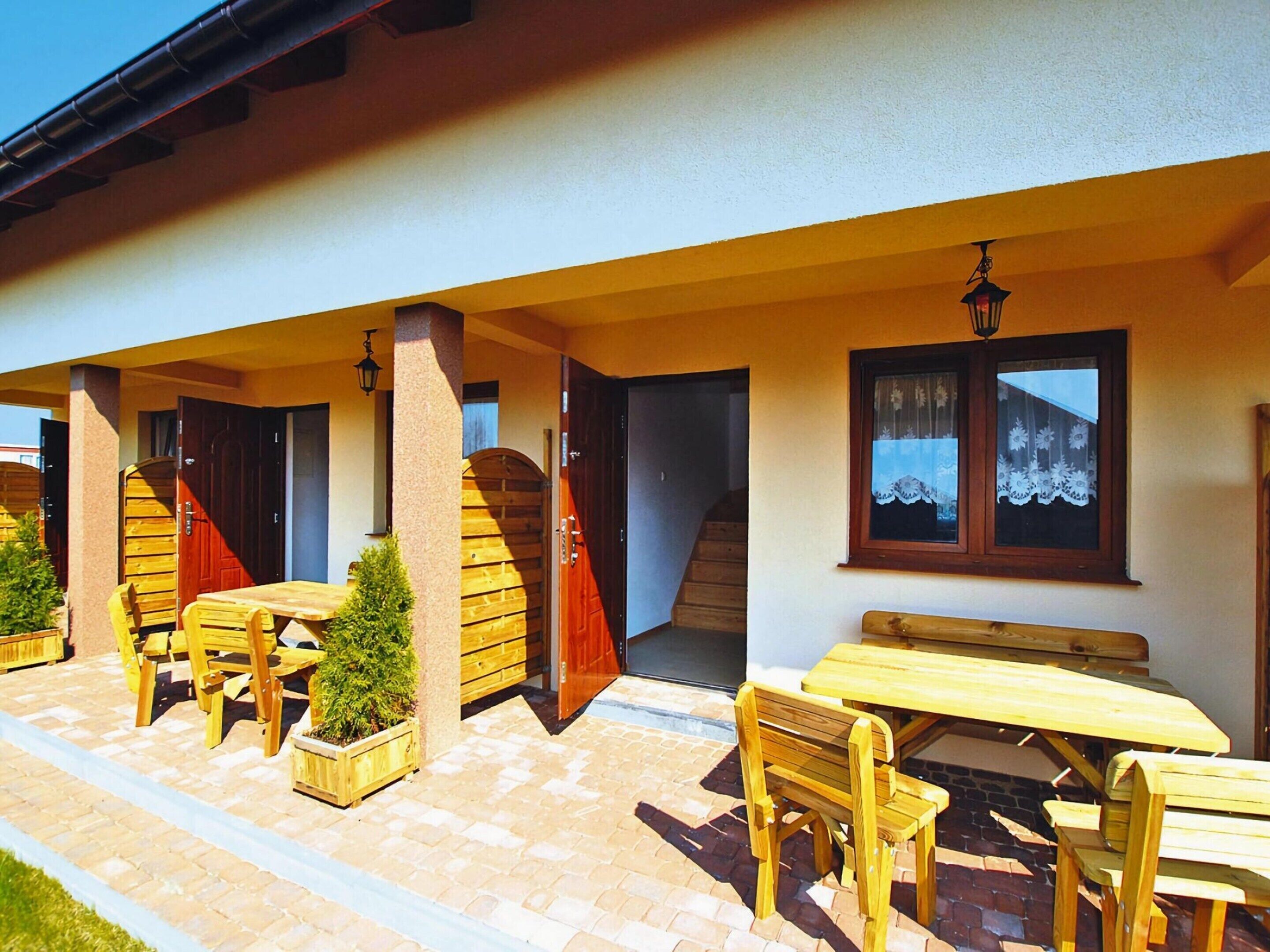 Eine Außenpatio-Terrasse mit Holzmöbeln, einem kleinen Topfpflanzen und einer Treppe, die zu einer oberen Ebene führt.