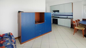 Ein gemütlicher Raum mit Bett, einem blauen Kleiderschrank, einer kleinen Küchenzeile und einem Essbereich mit Stühlen.