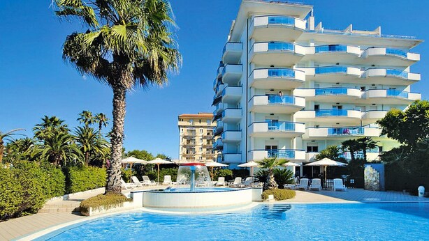 Ein Hotel mit Pool, Palmen und einem mehrstöckigen Gebäude mit Balkonen.
