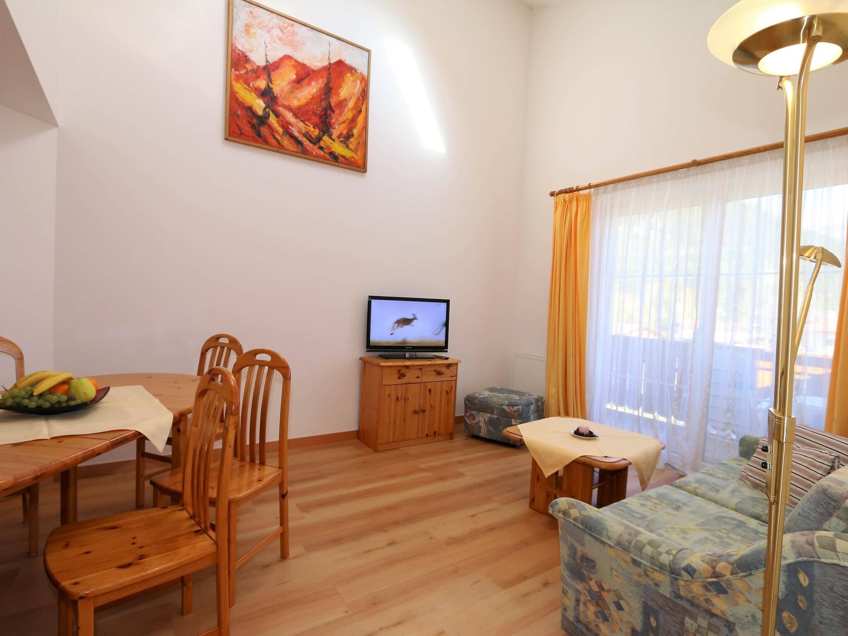 Una sala de estar con una mesa de comedor de madera, sillas, un televisor, un sofá y un cuadro en la pared.
