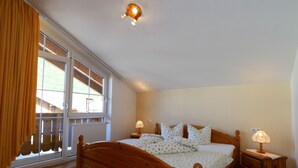 A bedroom with a wooden bed, two bedside tables with lamps, a window with curtains, and a ceiling light fixture. - Apartment in Bichlbach Near Zugspitze (Bichlbach)