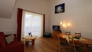 A living room with a red sofa, a wooden dining table with chairs, a television, and a painting on the wall. - Apartment in Bichlbach Near Zugspitze (Bichlbach)