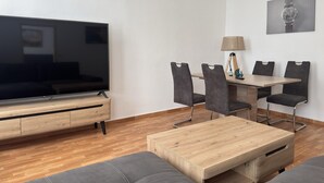 A modern living room with a flat-screen TV, a wooden coffee table, grey sofas, and a dining area with a table and chairs. - Ferienwohnung im Zentrum von Ballenstedt (Ballenstedt)