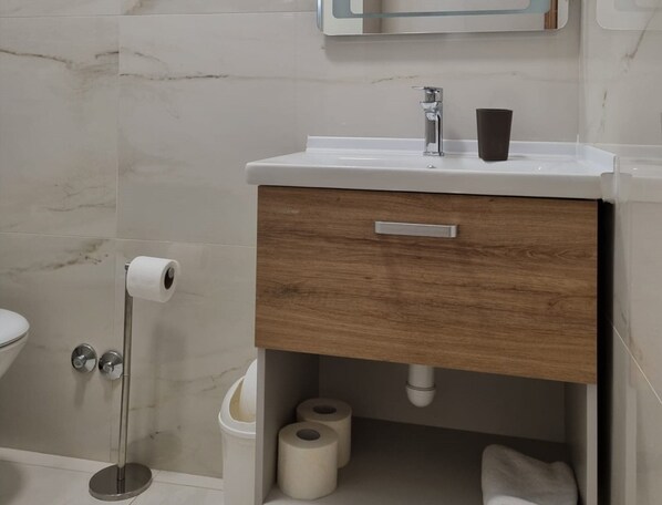 Une salle de bain avec un lavabo blanc, un meuble en bois et des toilettes.