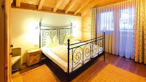 A bedroom with a wooden ceiling, a metal bed frame, a bedside table, a chair, and a window with curtains. - Chalet in Kitzbuhel Alps Near Hiking Trails (Wildschönau)