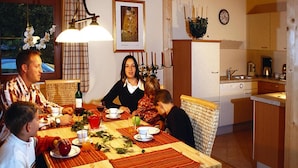 A family dining at a wooden table with placemats, surrounded by wicker chairs. A chandelier hangs above, and a framed painting is on the wall. - Chalet in Kitzbuhel Alps Near Hiking Trails (Wildschönau)