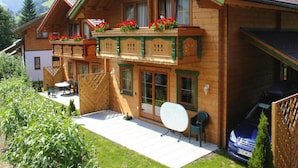 A wooden chalet with a balcony, a carport, and a patio area with a table and chairs. - Chalet in Kitzbuhel Alps Near Hiking Trails (Wildschönau)