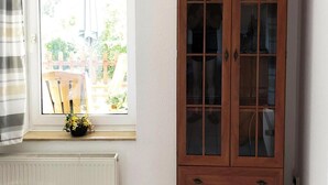 Une pièce avec une fenêtre, un radiateur, une armoire en bois et une chaise.