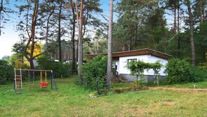 Une maison moderne, à l’extérieur blanc et au toit brun, entourée d’une cour verdoyante et d’arbres.