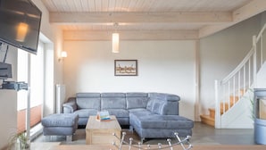 Ein modernes Wohnzimmer mit einem grauen Ecksofa, einem Holztisch und einem Metallregal.