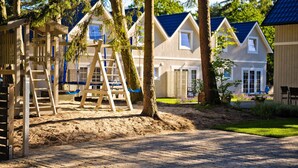Et boligområde med flere huse, en legeplads med gyngestativ og klatrestige, samt en belagt sti.