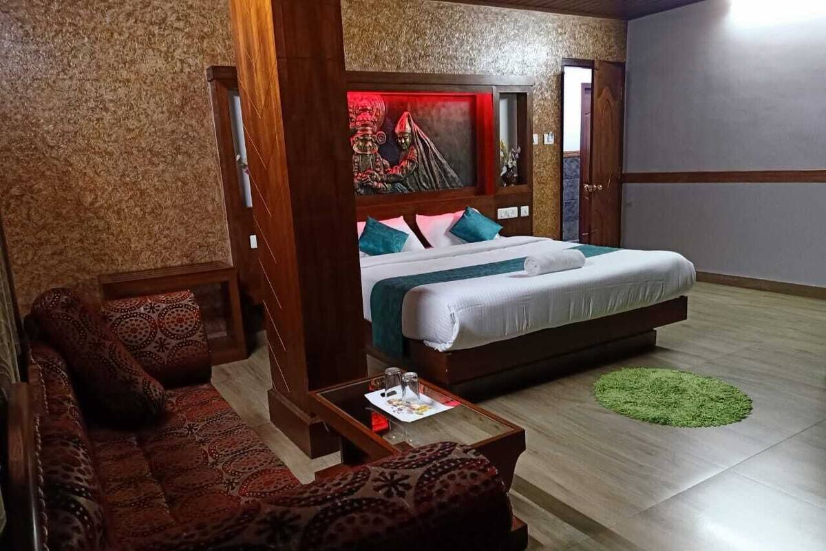 A hotel room with a large bed, a sofa, a small table, and a green rug.