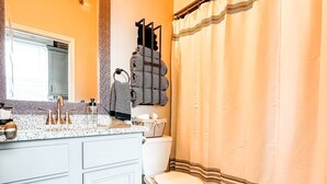Une salle de bain avec un meuble-lavabo blanc, un grand miroir, des toilettes et un rideau de douche.