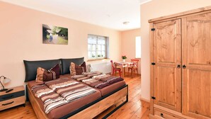 A bedroom with a large bed, a wooden wardrobe, a dining table with chairs, and a window. - Komfortable Wohnung in Lubben an der Spree (Lübben (Spreewald))