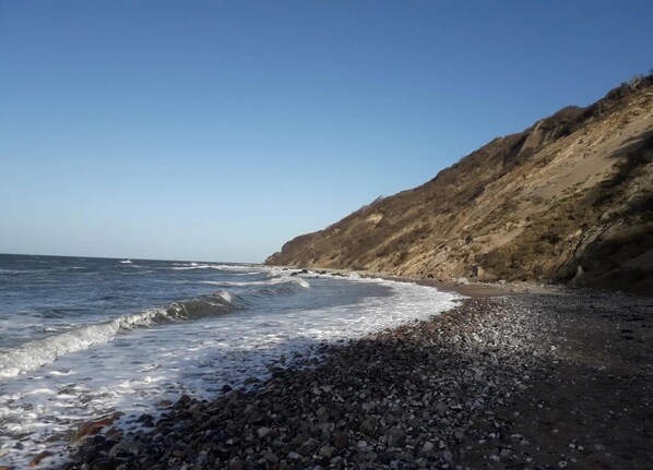 A rocky beach with waves crashing onto the shore and a steep cliff in the background. - Appartements Post Hiddensee, Vitte (Hiddensee)