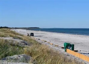 A beach with a sandy path, a parked car, and a green trash bin. - Appartements Post Hiddensee, Vitte (Hiddensee)