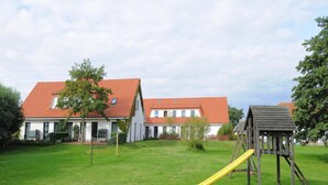 A residential area with two houses, a grassy yard, and a wooden play structure with a slide. - Appartements Post Hiddensee, Vitte (Hiddensee)