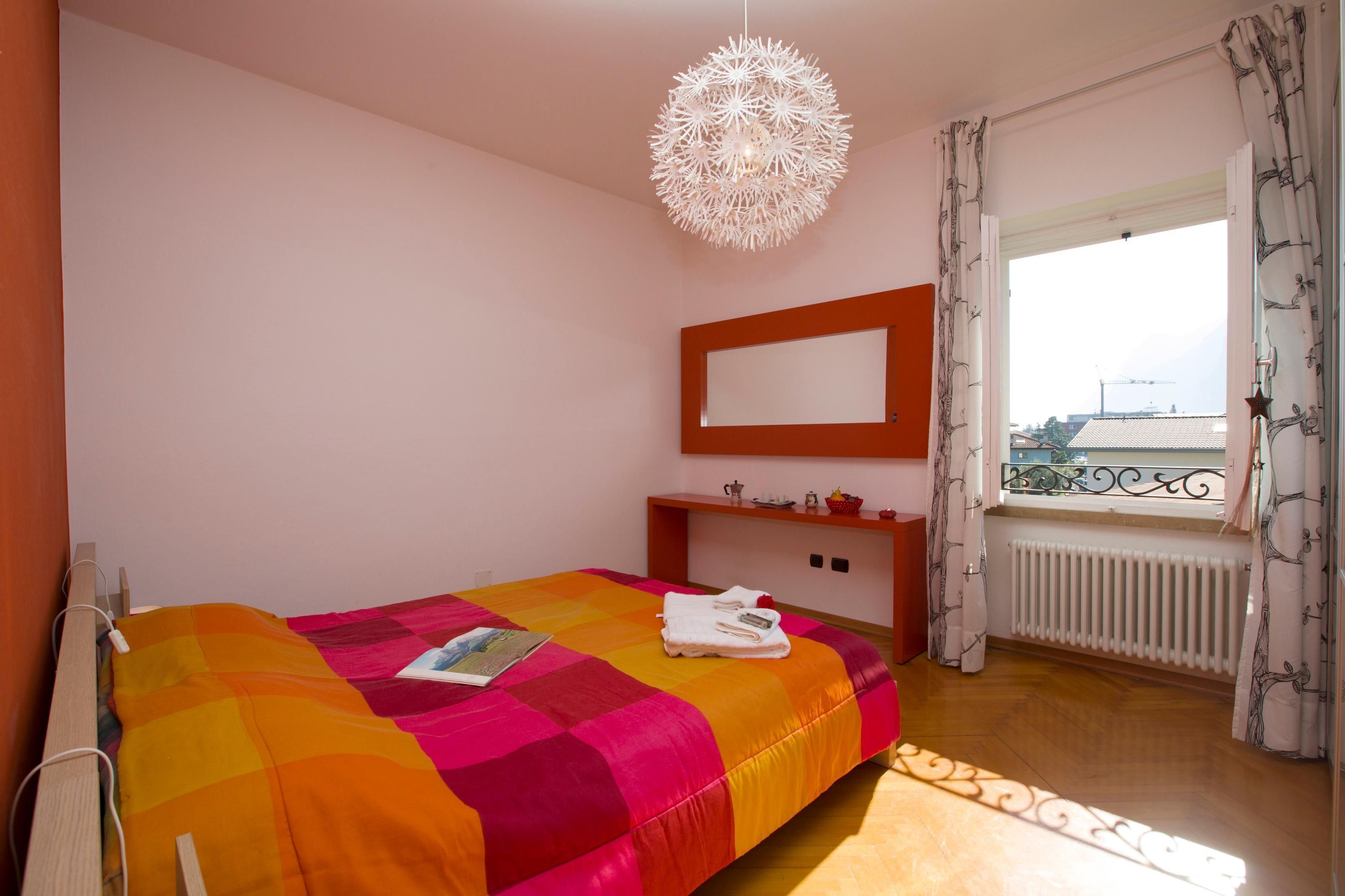 A bedroom with a bed, a bedside table, a mirror, and a window with curtains.