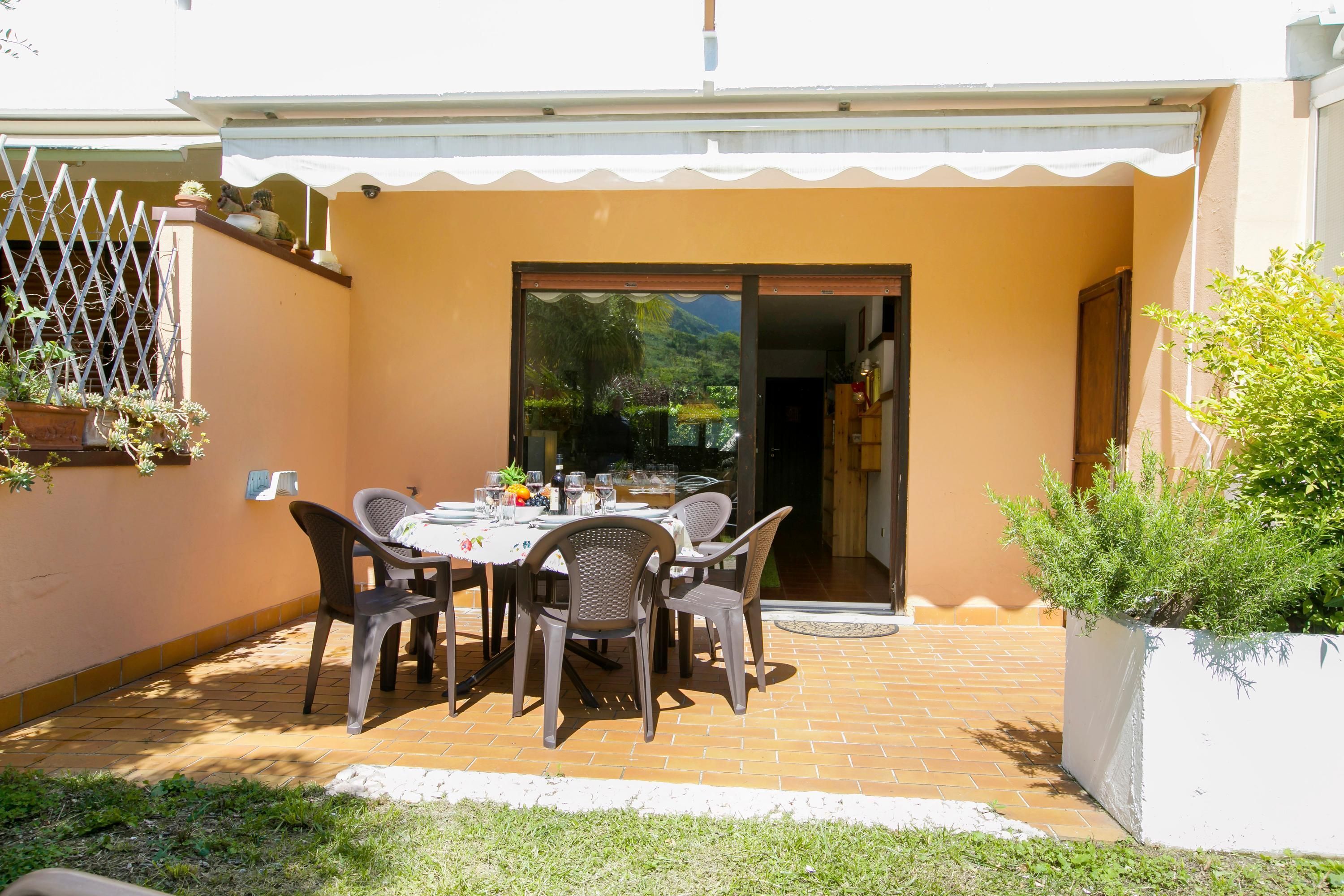 Un patio al aire libre con una mesa, sillas, barandal blanco y plantas en macetas.
